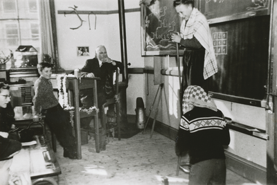 876412 Afbeelding van twee leerlingen uit een van de hogere klassen, die een stukje opvoeren in een versierd klaslokaal ...